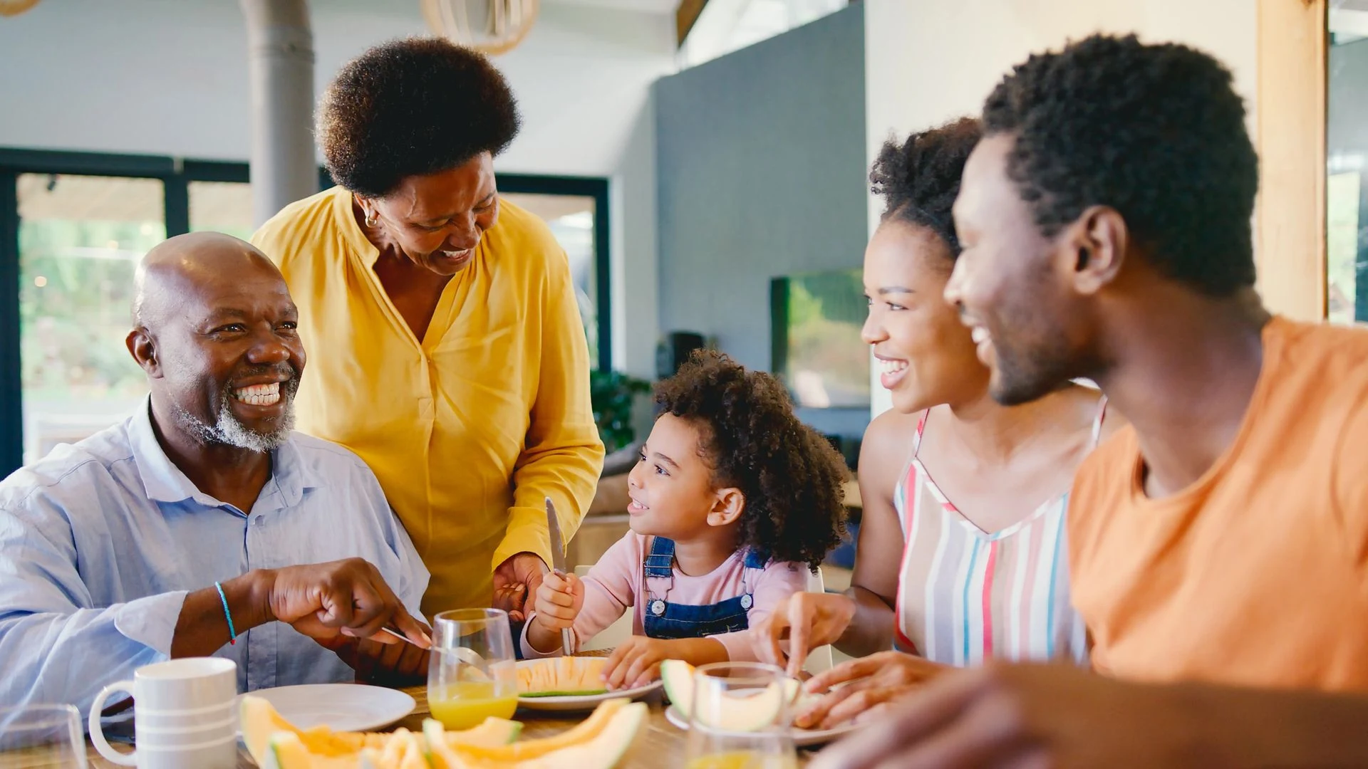 Grandparents, parents and a child laughing together around a breakfast table